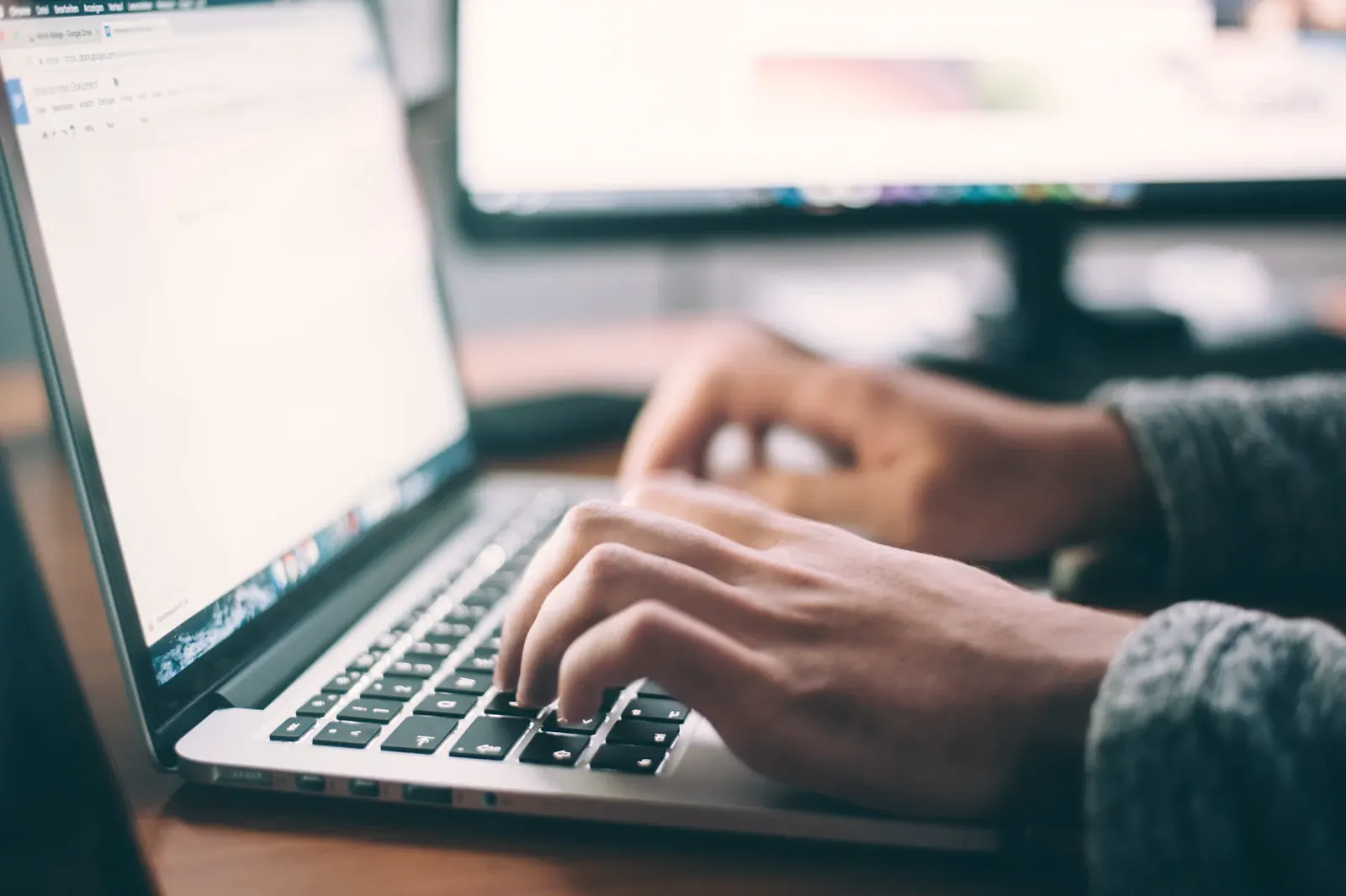 Hands at a laptop on a warm wooden desk, working through a website.